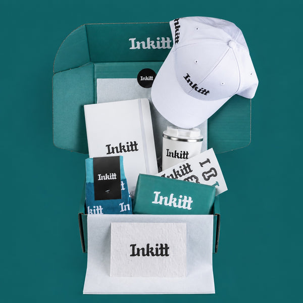 Inkitt branded swag box items, including a cap, mug, and cards on a teal background